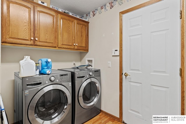 clothes washing area featuring washing machine and clothes dryer, light wood-type flooring, a textured ceiling, and cabinets