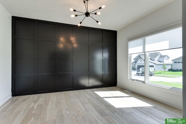 spare room with a notable chandelier and light hardwood / wood-style flooring