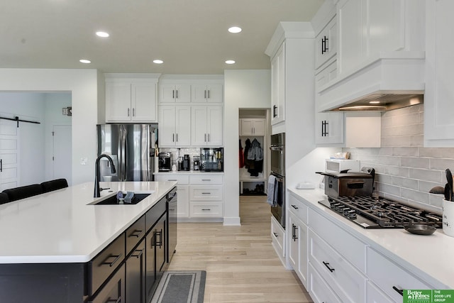 kitchen featuring a kitchen island with sink, a barn door, appliances with stainless steel finishes, sink, and white cabinetry