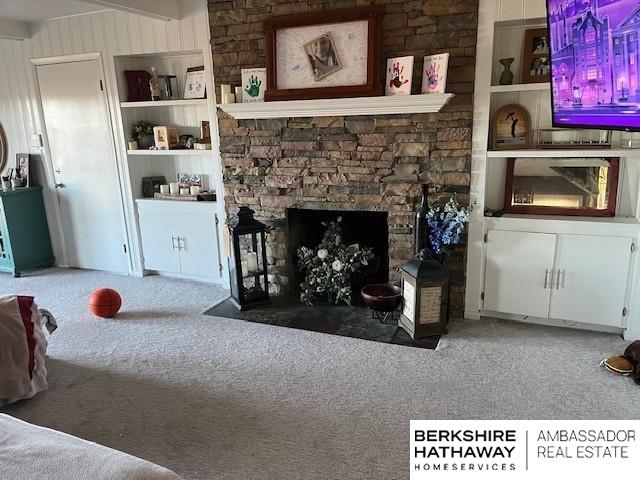 carpeted living room with built in shelves, beamed ceiling, and a fireplace