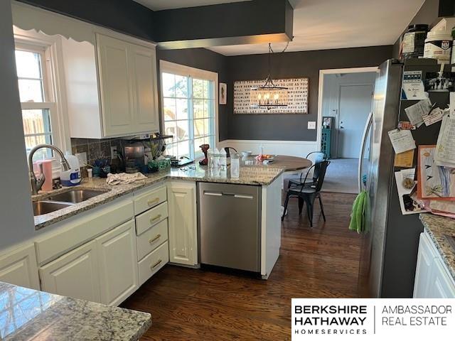 kitchen with stainless steel appliances, dark wood-type flooring, white cabinets, light stone counters, and sink