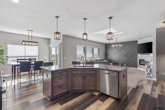 kitchen featuring sink, stainless steel dishwasher, hanging light fixtures, a center island with sink, and a stone fireplace