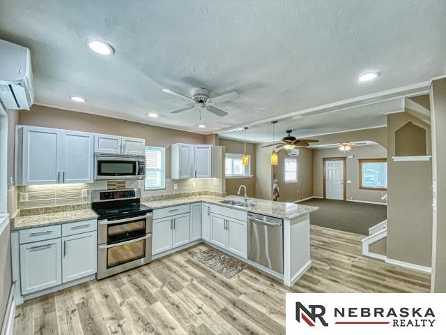 kitchen with appliances with stainless steel finishes, kitchen peninsula, sink, white cabinets, and tasteful backsplash