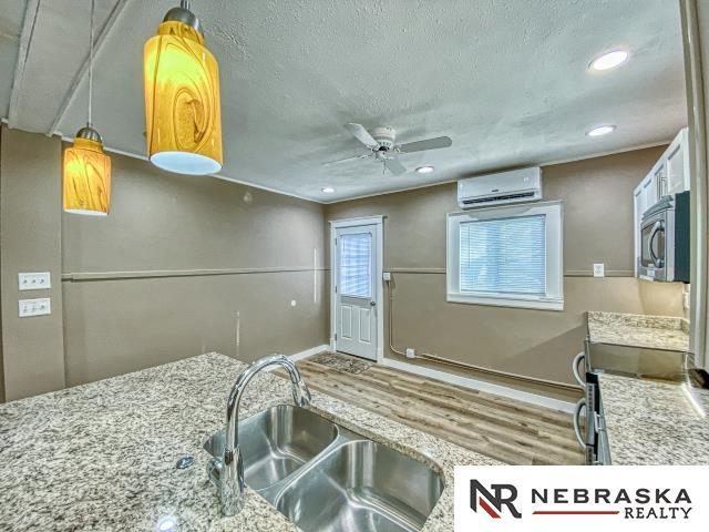 kitchen featuring a textured ceiling, a wall unit AC, hanging light fixtures, wood-type flooring, and sink