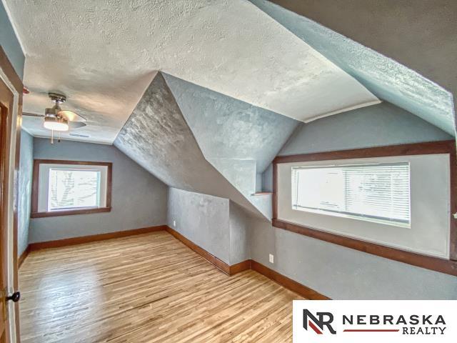 additional living space featuring lofted ceiling, a textured ceiling, light hardwood / wood-style floors, and a wealth of natural light