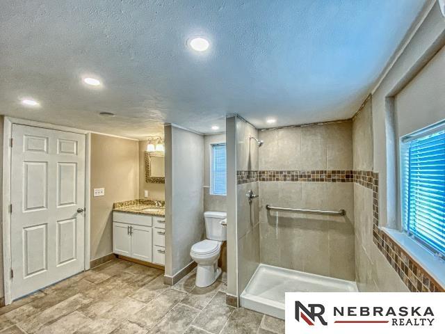 bathroom with toilet, a textured ceiling, a wealth of natural light, a tile shower, and vanity