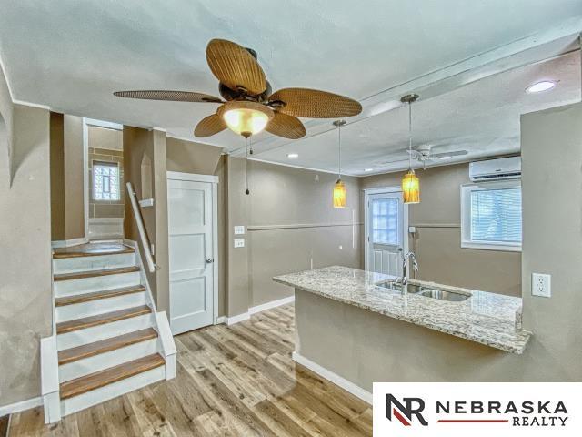 kitchen featuring light wood-type flooring, pendant lighting, a wall mounted air conditioner, light stone counters, and sink