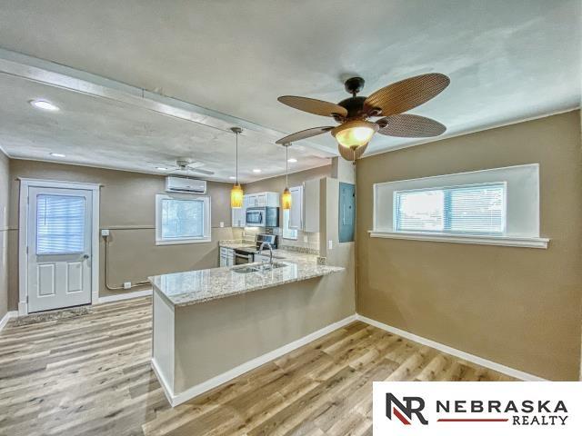 kitchen with stainless steel appliances, light wood-type flooring, kitchen peninsula, hanging light fixtures, and light stone countertops