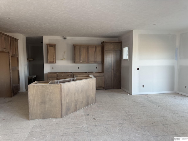 kitchen featuring baseboards, a textured ceiling, brown cabinets, and a center island