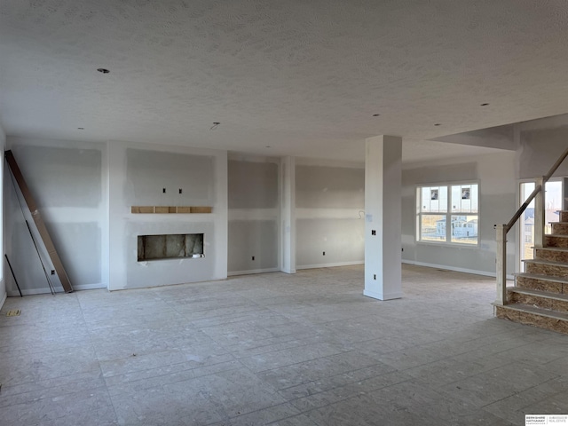 unfurnished living room featuring stairway, a fireplace, a textured ceiling, and baseboards