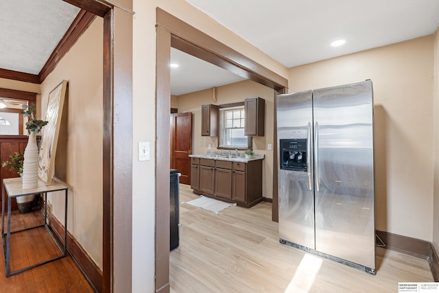 kitchen with sink, light stone counters, light wood-type flooring, stainless steel refrigerator with ice dispenser, and crown molding