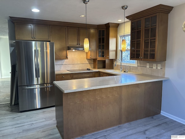 kitchen featuring kitchen peninsula, decorative light fixtures, light wood-type flooring, stainless steel refrigerator, and sink