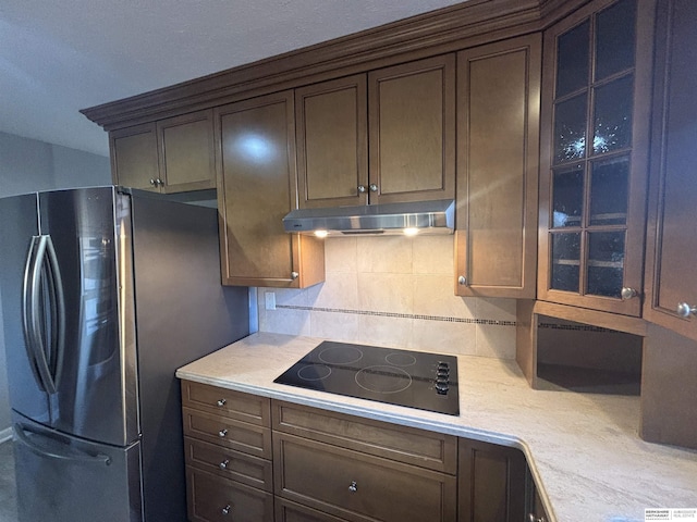 kitchen with stainless steel refrigerator, backsplash, dark brown cabinets, and black electric cooktop