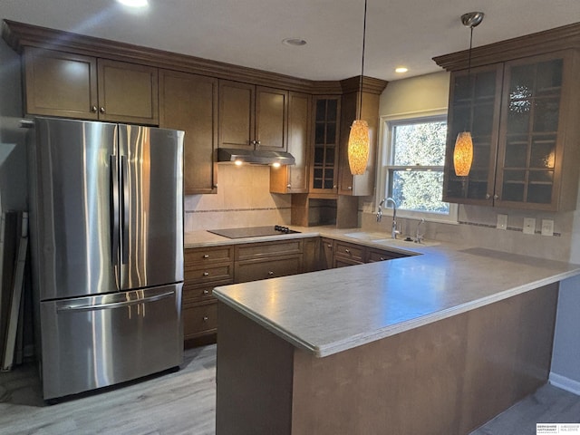 kitchen featuring light wood-type flooring, kitchen peninsula, stainless steel fridge, pendant lighting, and sink