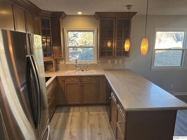 kitchen with kitchen peninsula, stainless steel fridge, pendant lighting, hardwood / wood-style flooring, and sink