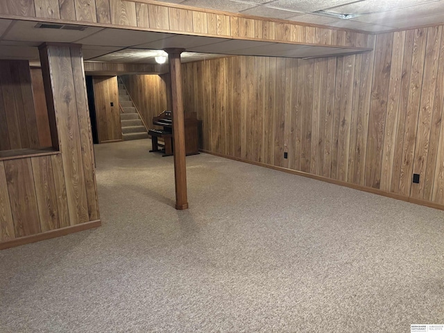 basement featuring wood walls, a drop ceiling, and light colored carpet