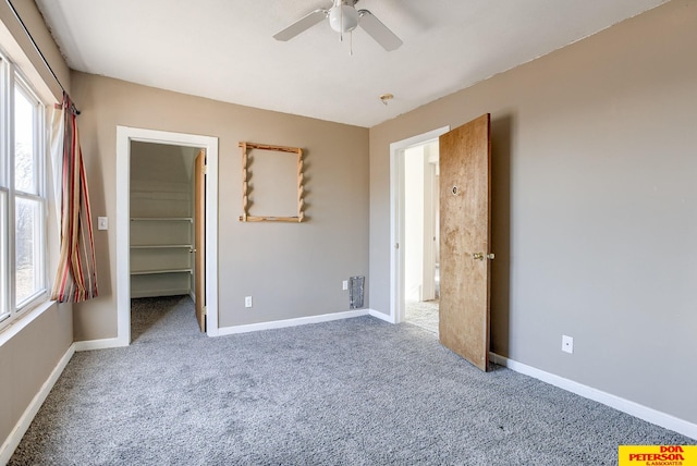 unfurnished bedroom featuring a closet, multiple windows, carpet floors, a walk in closet, and ceiling fan