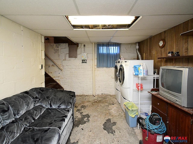 basement with a paneled ceiling, washer and clothes dryer, and wood walls