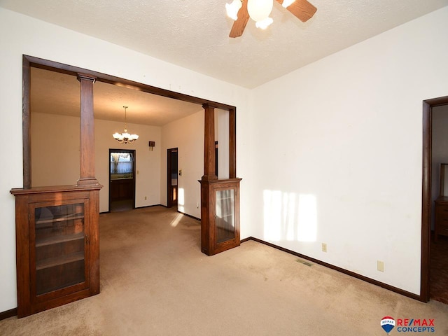 carpeted empty room featuring a textured ceiling, ceiling fan with notable chandelier, and ornate columns