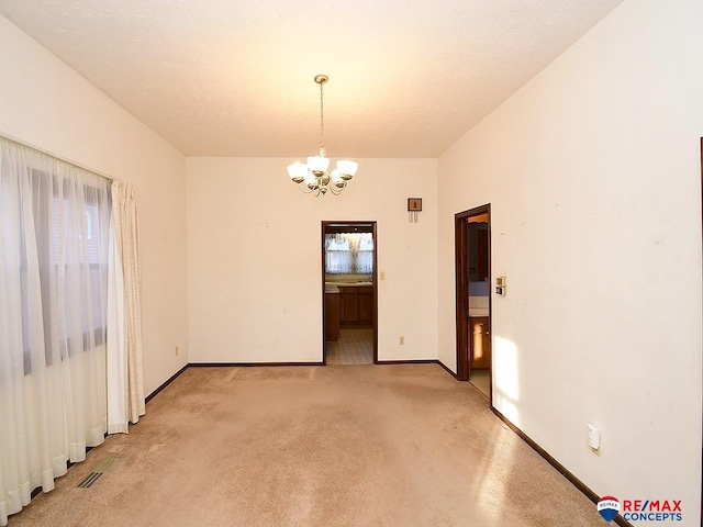 empty room featuring a wealth of natural light, light carpet, a chandelier, and a textured ceiling