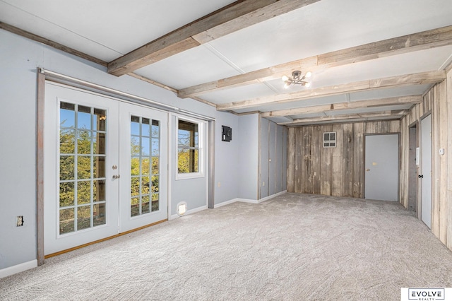 carpeted empty room featuring an inviting chandelier, french doors, wooden walls, and beamed ceiling