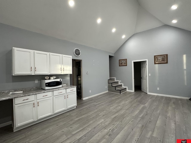 kitchen featuring high vaulted ceiling, white cabinets, and light stone countertops