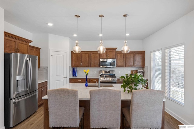 kitchen with stainless steel appliances, backsplash, hanging light fixtures, and a kitchen island with sink