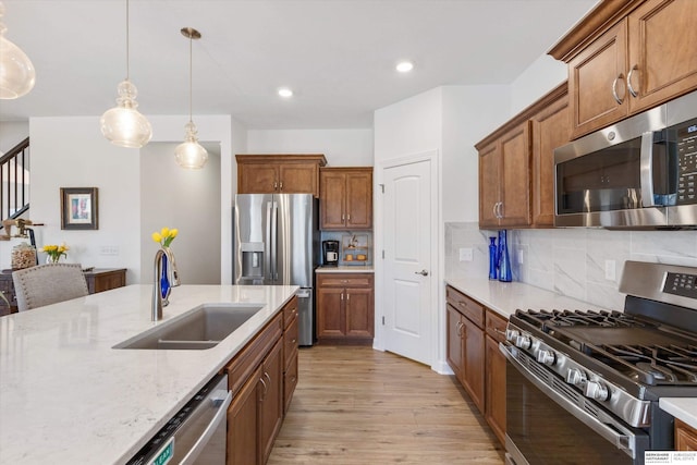 kitchen featuring backsplash, sink, hanging light fixtures, light wood-type flooring, and appliances with stainless steel finishes