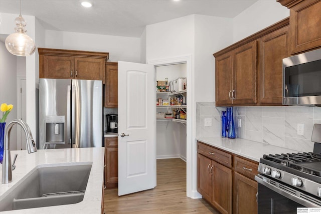 kitchen featuring appliances with stainless steel finishes, tasteful backsplash, decorative light fixtures, light wood-type flooring, and sink