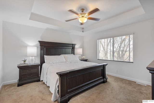 carpeted bedroom with ceiling fan and a tray ceiling