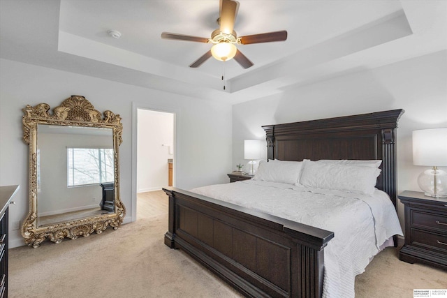 bedroom featuring light carpet, ceiling fan, ensuite bathroom, and a tray ceiling