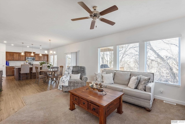 living room featuring light wood-type flooring, plenty of natural light, and ceiling fan with notable chandelier