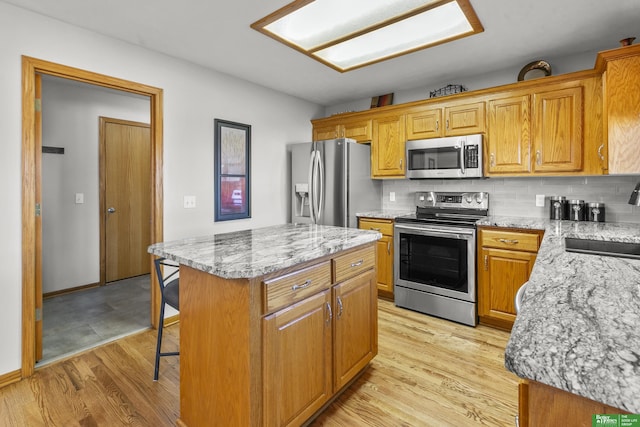 kitchen with sink, a center island, light stone counters, backsplash, and appliances with stainless steel finishes