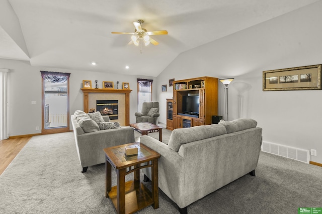 living room with ceiling fan, a tiled fireplace, and vaulted ceiling