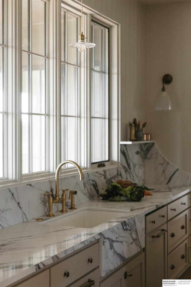 kitchen featuring sink, decorative light fixtures, and light stone countertops