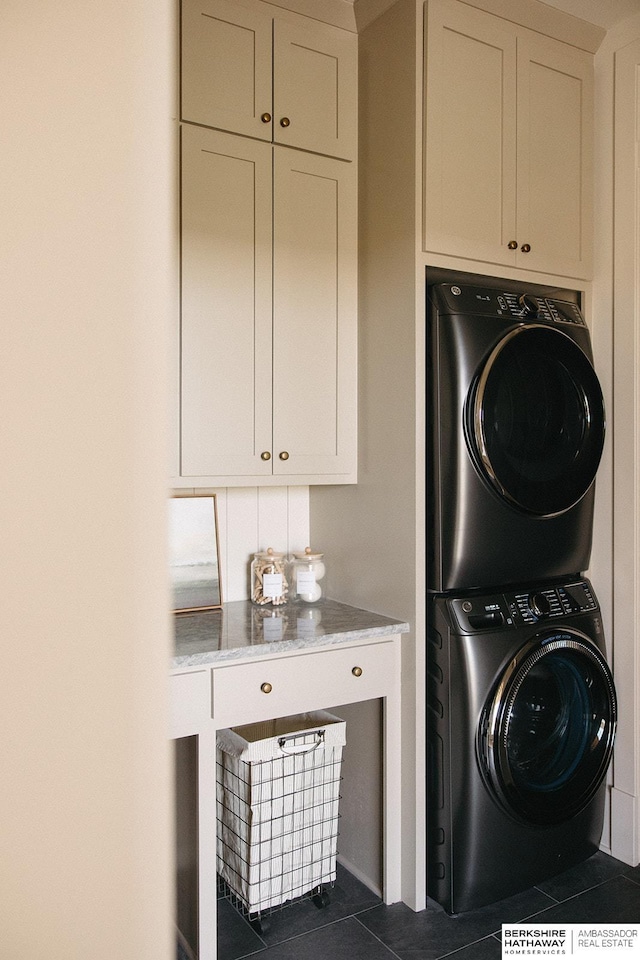 washroom featuring stacked washing maching and dryer, cabinets, and dark tile patterned flooring