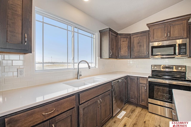 kitchen featuring stainless steel appliances, decorative backsplash, sink, light hardwood / wood-style flooring, and lofted ceiling