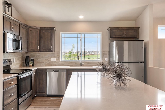 kitchen with appliances with stainless steel finishes, dark brown cabinetry, backsplash, and sink