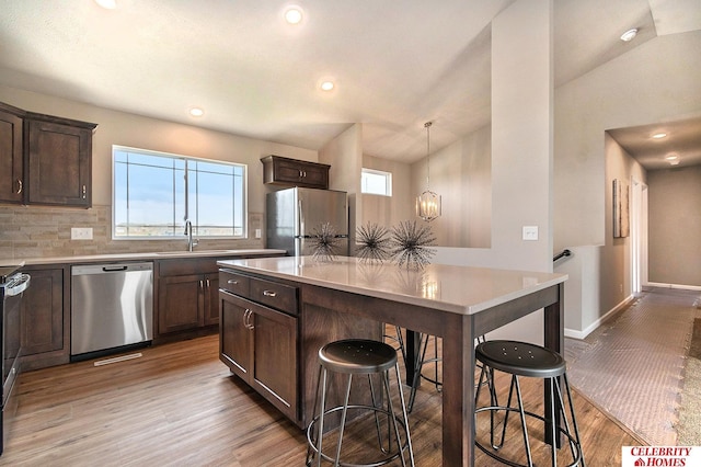 kitchen with decorative light fixtures, stainless steel appliances, backsplash, a kitchen breakfast bar, and sink