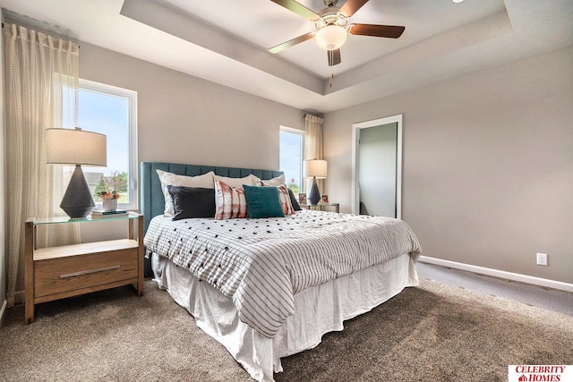 bedroom with dark carpet, ceiling fan, and a tray ceiling