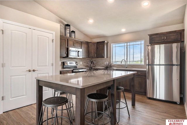 kitchen with stainless steel appliances, light wood-type flooring, dark brown cabinetry, sink, and lofted ceiling