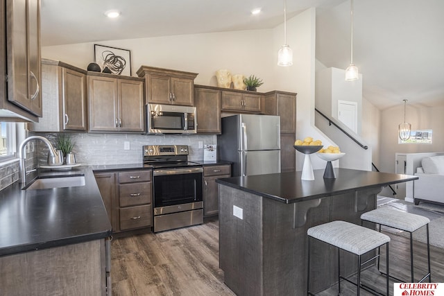 kitchen with vaulted ceiling, stainless steel appliances, a kitchen island, sink, and backsplash