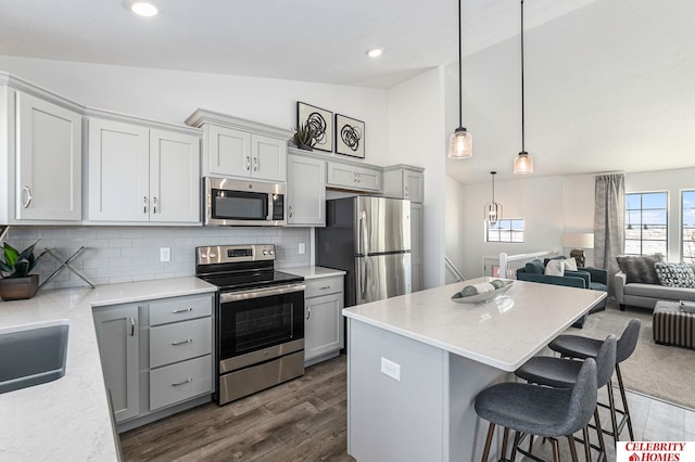 kitchen with stainless steel appliances, vaulted ceiling, a kitchen bar, tasteful backsplash, and pendant lighting