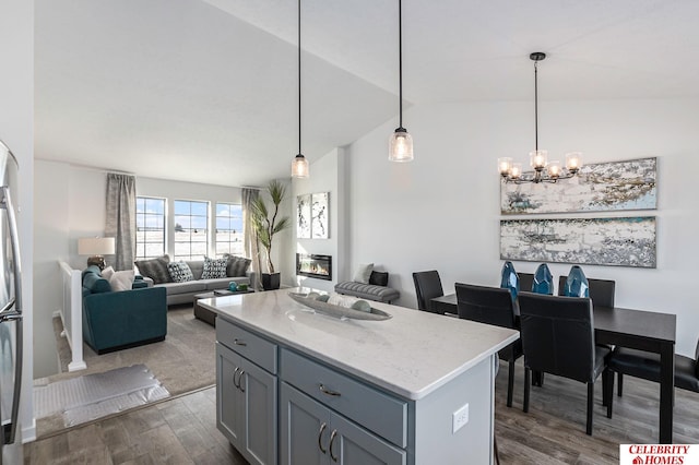 kitchen with an inviting chandelier, vaulted ceiling, a kitchen island, pendant lighting, and dark wood-type flooring