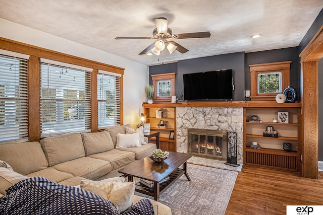 living room featuring a healthy amount of sunlight, a textured ceiling, wood-type flooring, and a stone fireplace