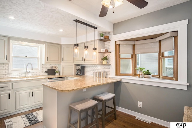 kitchen featuring sink, a kitchen breakfast bar, kitchen peninsula, backsplash, and light stone countertops