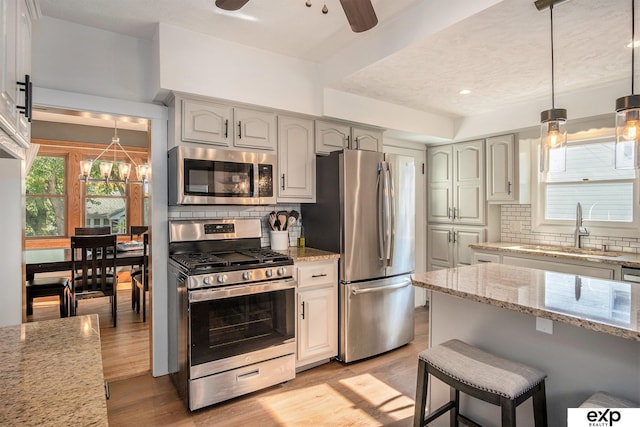 kitchen with stainless steel appliances, ceiling fan, tasteful backsplash, and light stone countertops