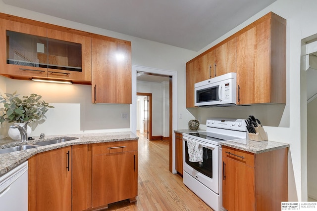 kitchen featuring sink, white appliances, light wood-type flooring, and light stone counters