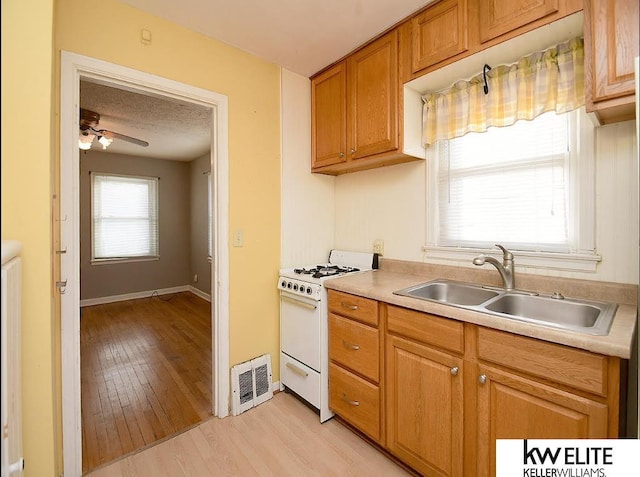 kitchen featuring a textured ceiling, light wood-type flooring, gas range gas stove, ceiling fan, and sink