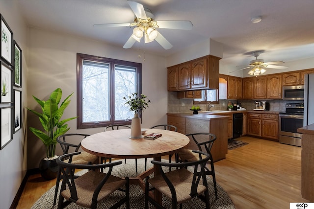 kitchen with light wood-type flooring, ceiling fan, appliances with stainless steel finishes, and decorative backsplash